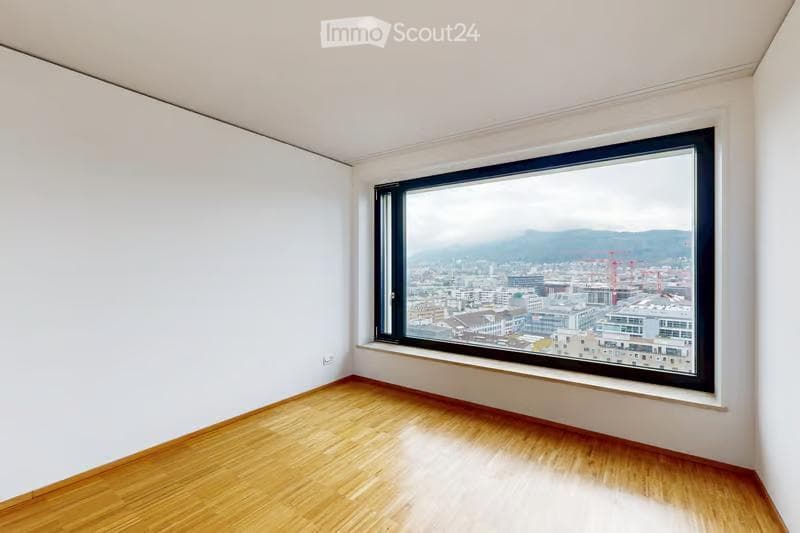 Empty room with wooden flooring and large window offering a cityscape view.