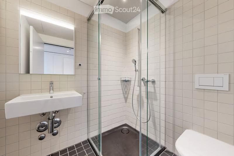 Modern bathroom with white tiles, a glass-enclosed shower, a white sink, and a mirror above it.