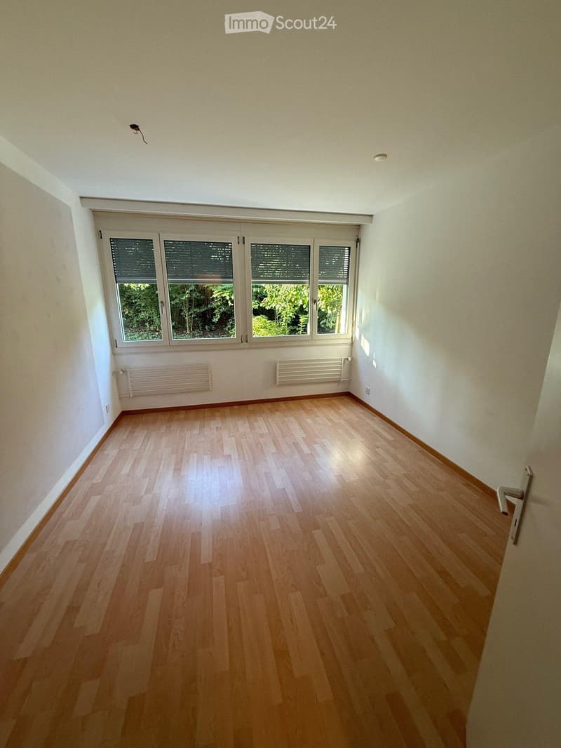 Empty room with wooden flooring, white walls, large windows with blinds, and radiators on the walls.
