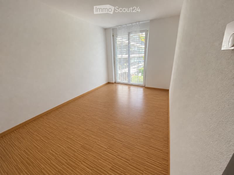 Empty room with wooden flooring and white walls, featuring a large sliding glass door with blinds leading to a balcony.