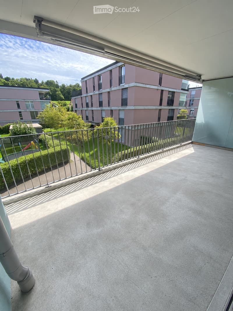 Balcony with modern railing, concrete floor, and view of a residential building and greenery.
