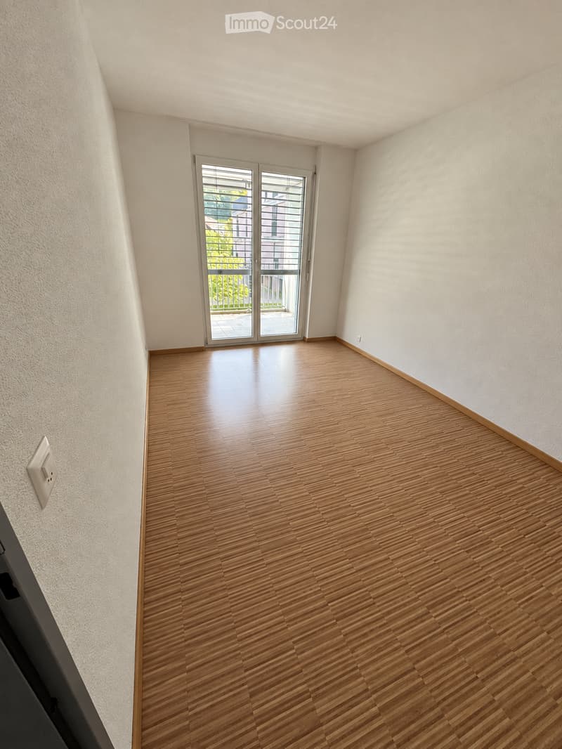 Empty room with wooden flooring, white walls, and a large sliding glass door leading to a balcony.