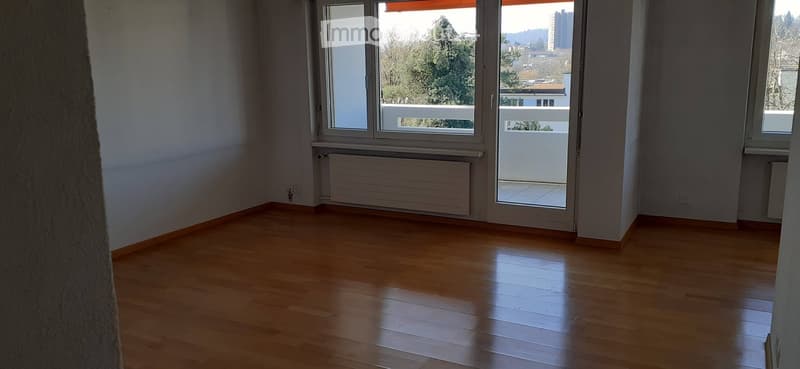 Empty room with wooden flooring, large windows, and a balcony access door.