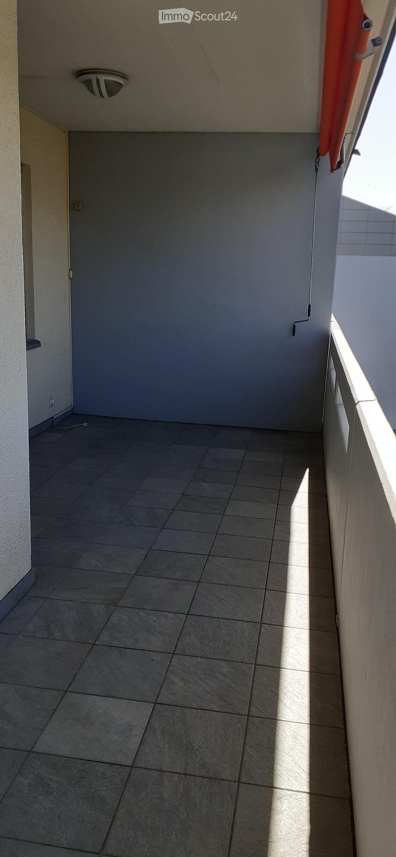 Empty balcony with tiled floor, white walls, and a closed window with an orange curtain partially visible.