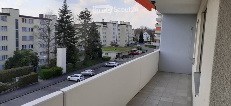 Balcony overlooking a residential area with parked cars, greenery, and apartment buildings.