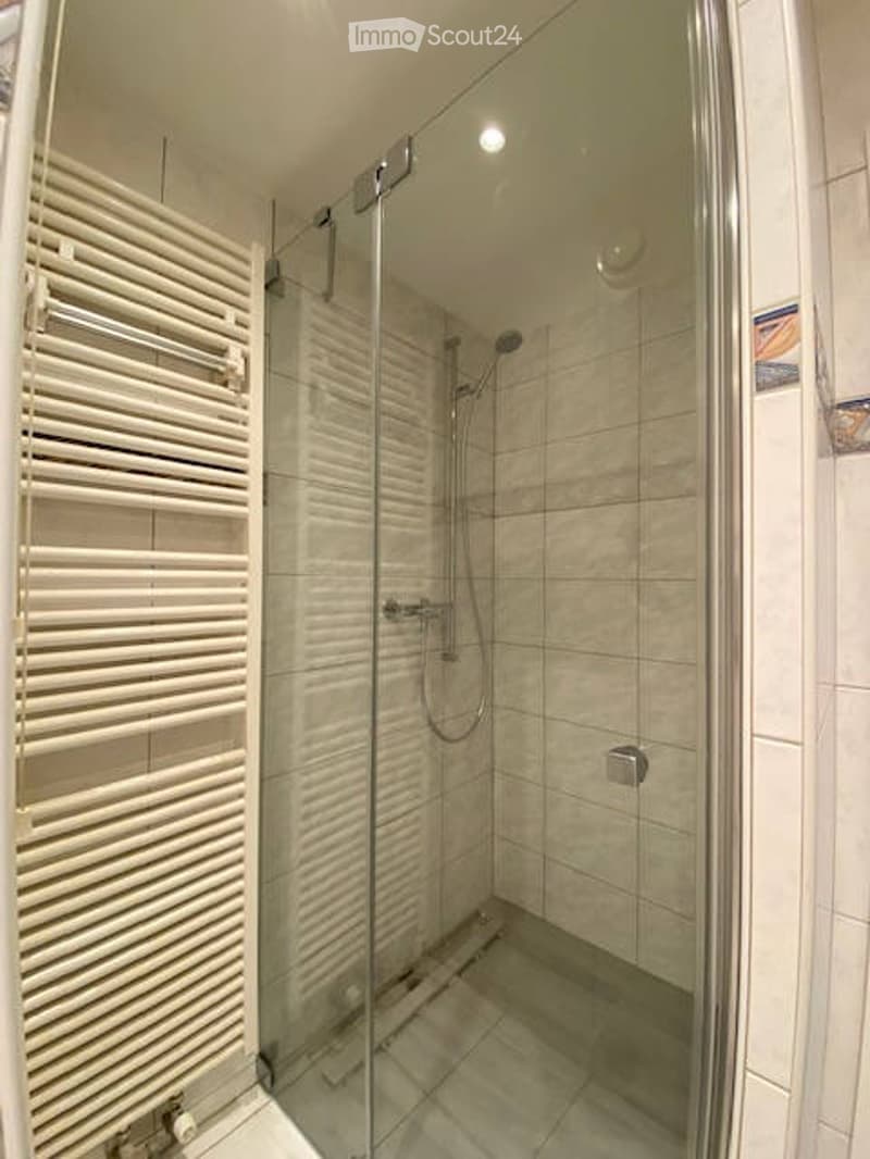 Modern bathroom with a glass-enclosed shower, a towel rack, and tiled walls and floor.