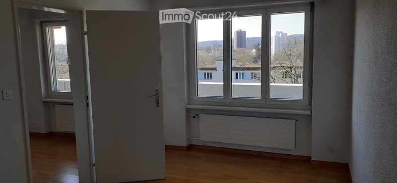 Empty room with wooden flooring, white walls, large windows, and a radiator below one window. No furniture or personal items are present.