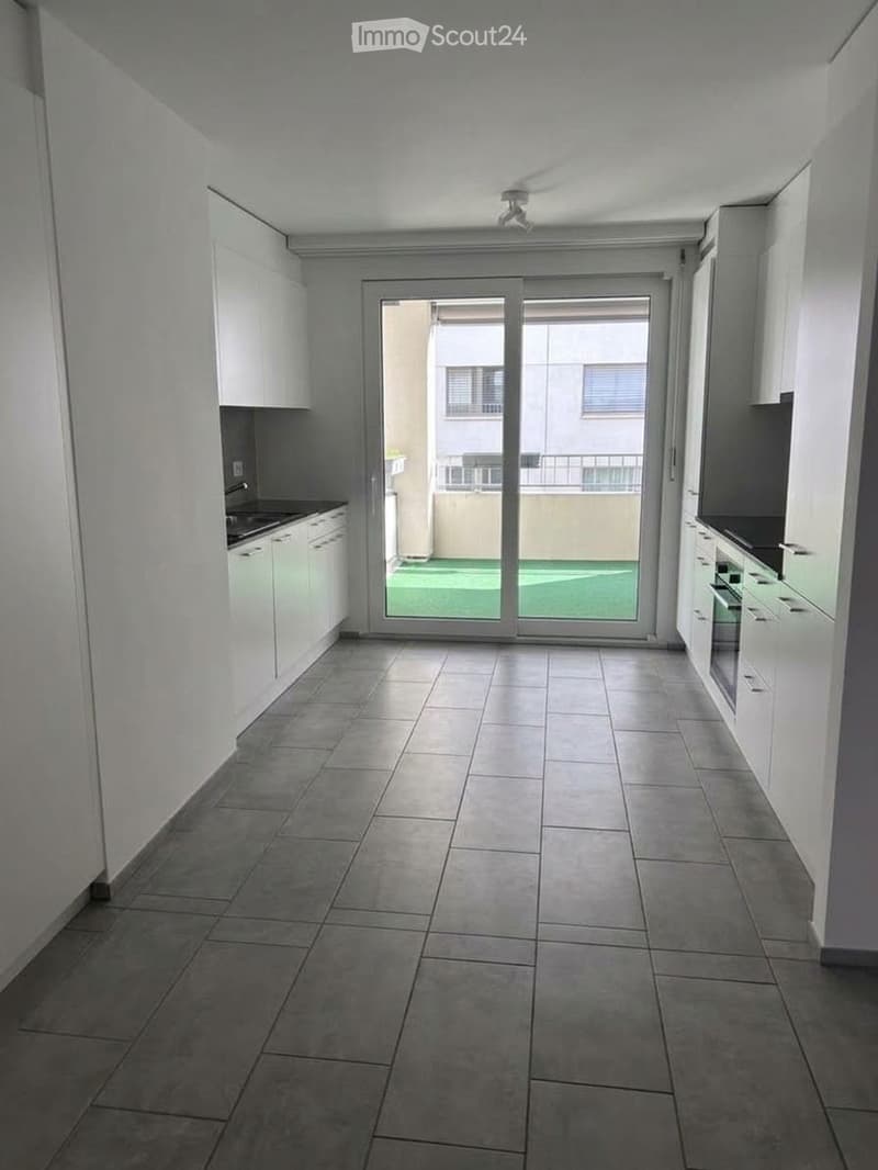 Empty kitchen with white cabinets, tiled floor, and a sliding glass door leading to a balcony.