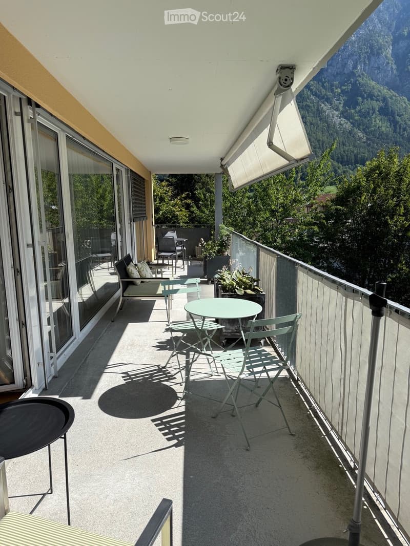Balcony with a scenic mountain view, featuring a round table, chairs, and a sofa.