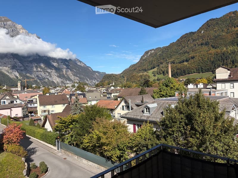 Balcony overlooking a town with houses, trees, and mountains in the background.