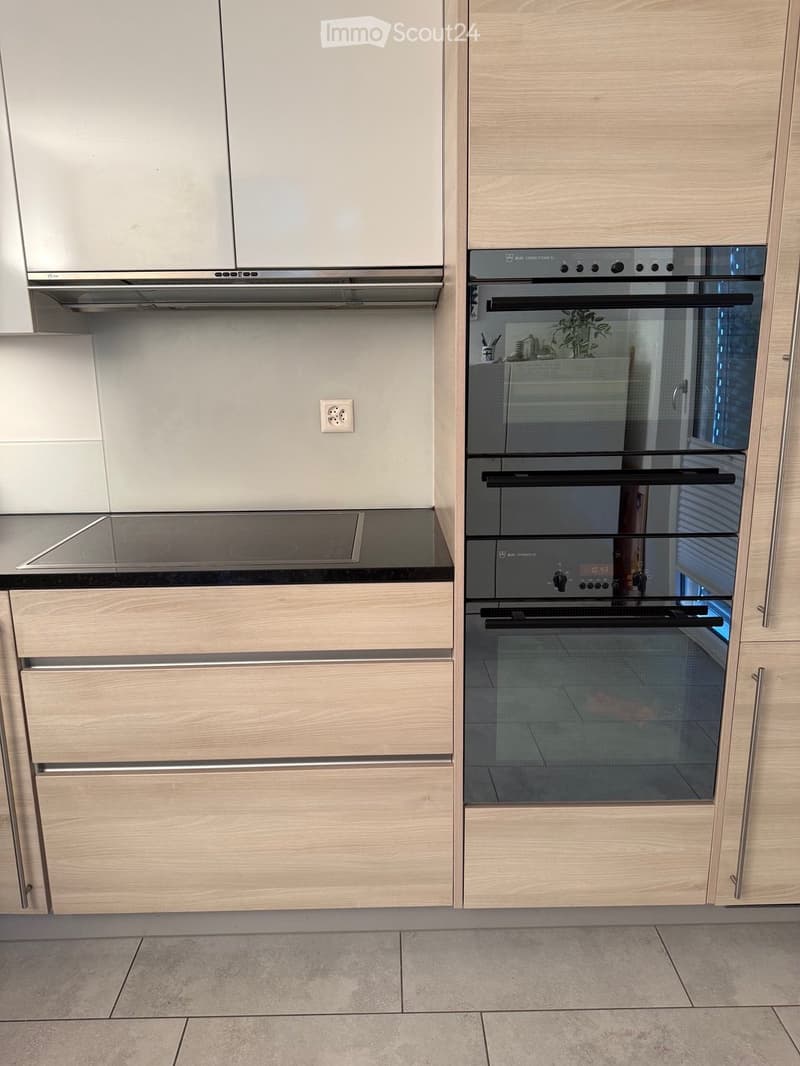Modern kitchen with light wooden cabinets, stainless steel oven, induction cooktop, and range hood.