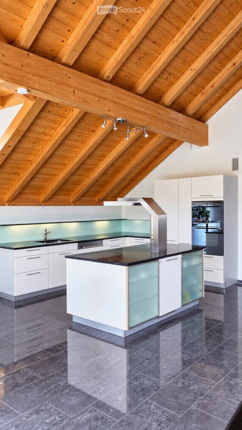 Modern kitchen with white cabinets, black countertops, and a central island. Features a sleek design with stainless steel appliances and a wooden ceiling.