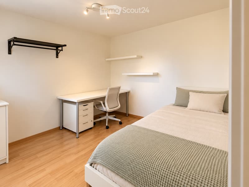 A modern, minimalist bedroom with a single bed, a desk with a chair, and built-in shelves. The room features light-colored walls, wooden flooring, and a sleek, contemporary design.