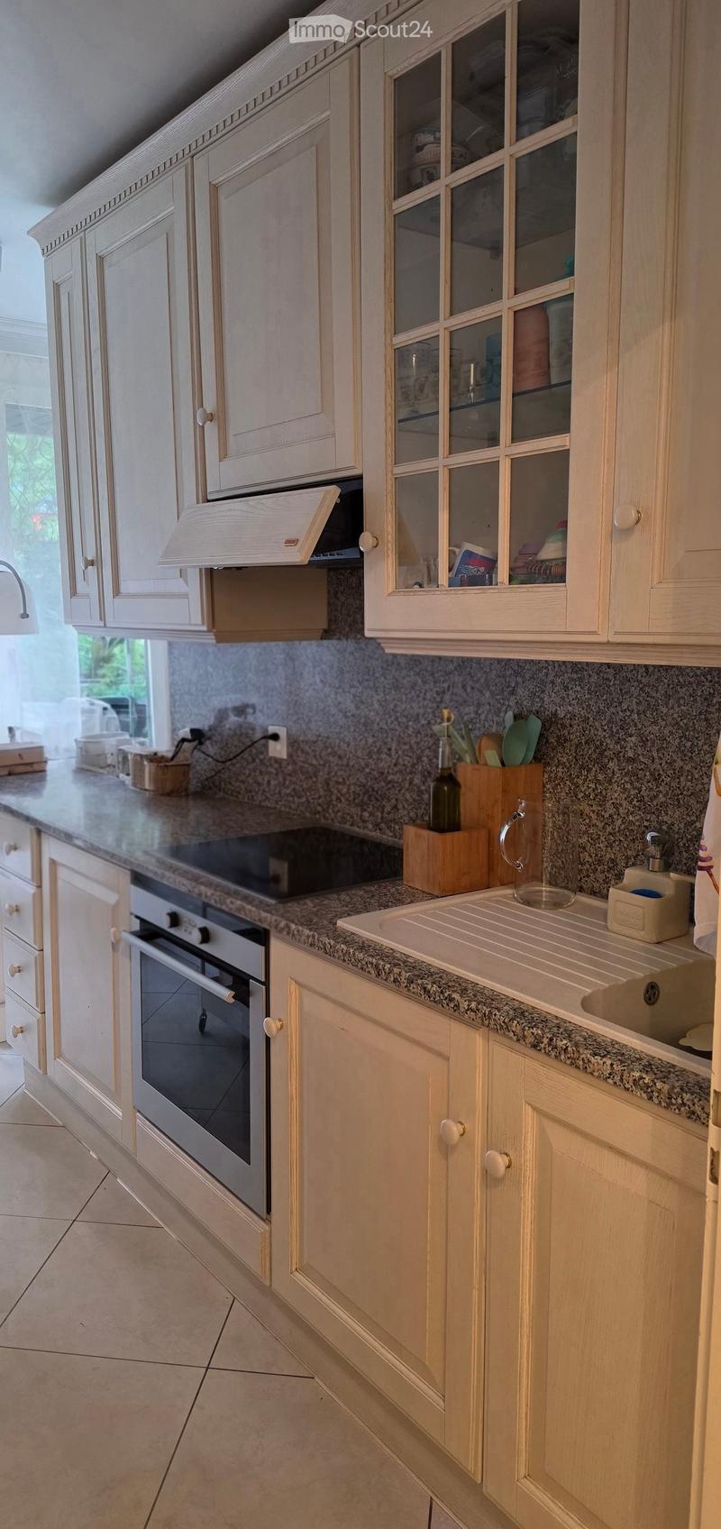 A modern kitchen with light wooden cabinets, granite countertops, and stainless steel appliances including an oven and sink.