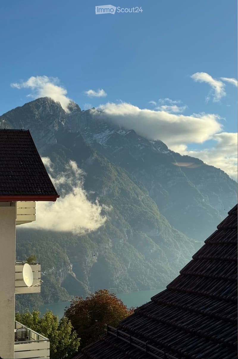 View from a balcony showing a mountain range, a lake, and a partly cloudy sky.