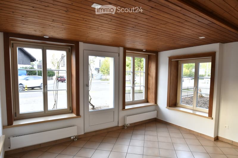 Empty room with tiled floor, white walls, wooden ceiling, and multiple windows with radiators beneath them.