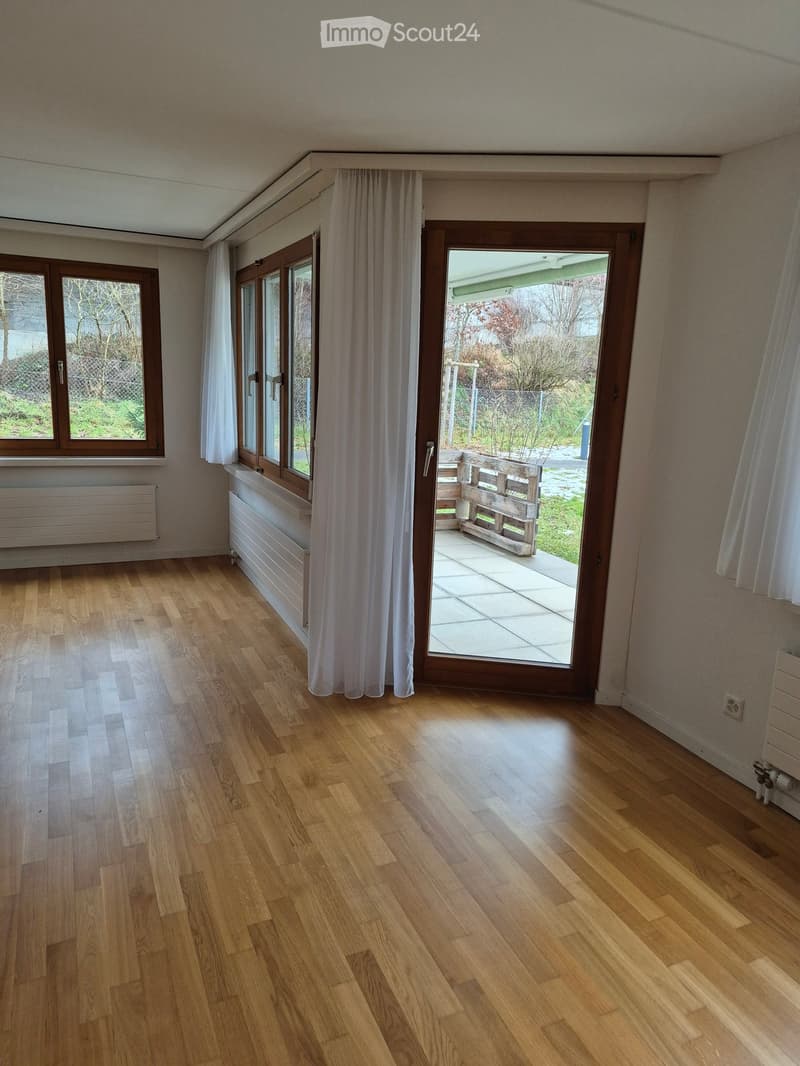 Empty room with wooden flooring, large windows, and a sliding glass door leading to a patio area.