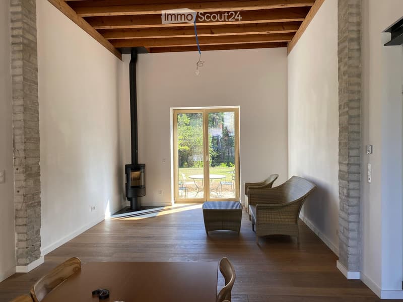 Bright living room with wooden floors, exposed wooden ceiling beams, fireplace, large sliding glass doors leading to outdoor seating area.