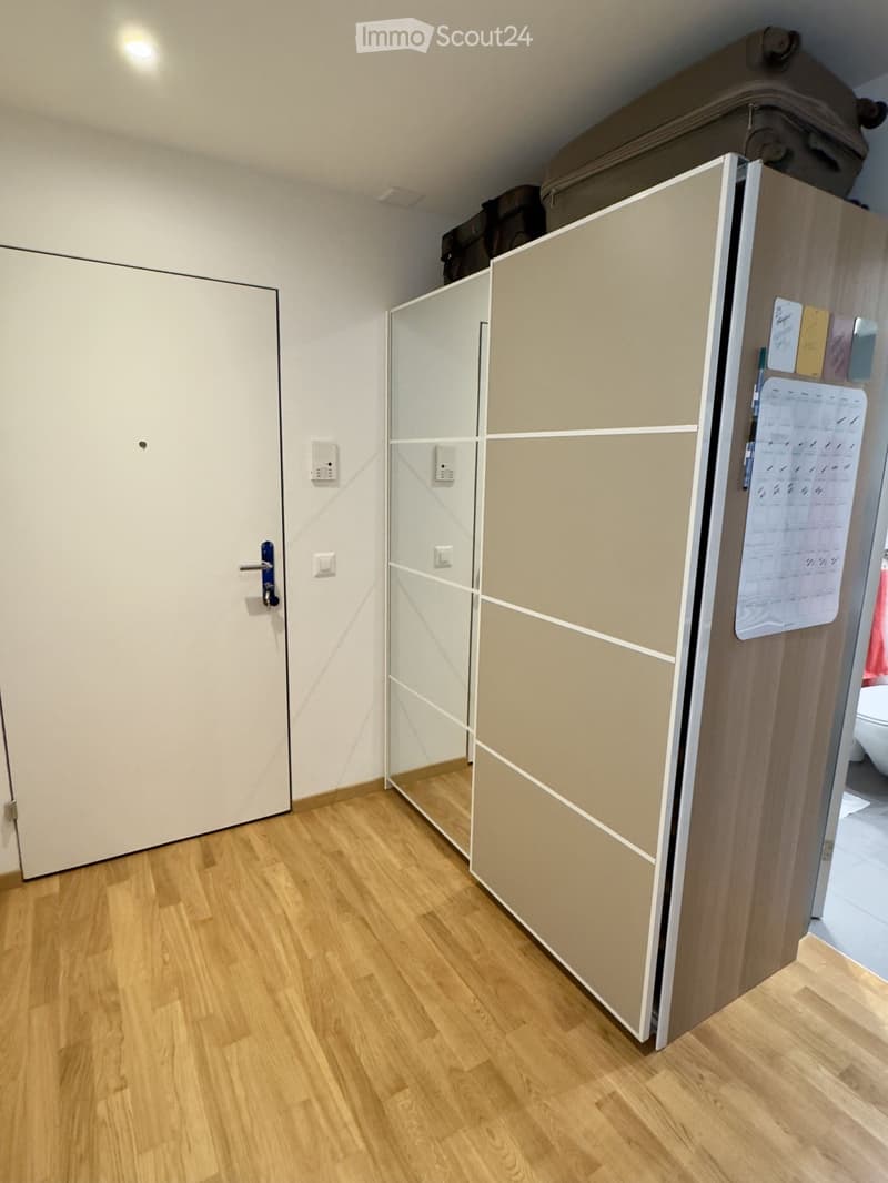 Empty room with wooden flooring, white walls, and a large sliding closet door. A small section of another room is visible in the background.