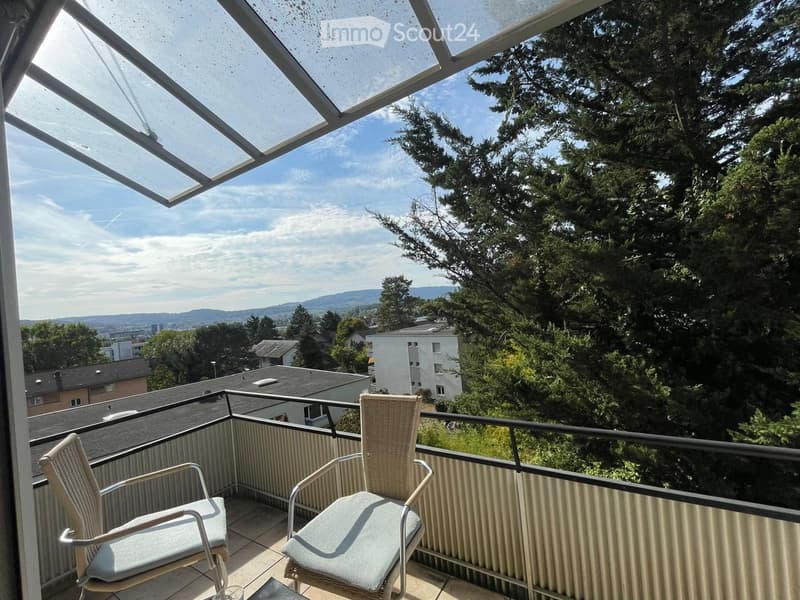 Balcony with two wicker chairs, metal railing, and a view of trees and cityscape.