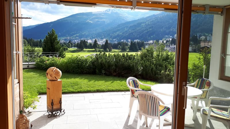 Balcony with a round table and four chairs, overlooking a green lawn and distant mountains.