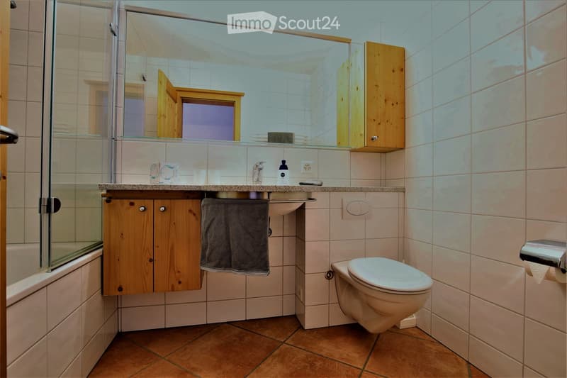 Modern bathroom with a toilet, sink, mirror, wooden cabinet, and a glass-enclosed shower area.