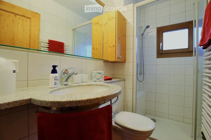 Modern bathroom with white tiles, granite countertop, sink, toilet, shower, and wooden cabinets.