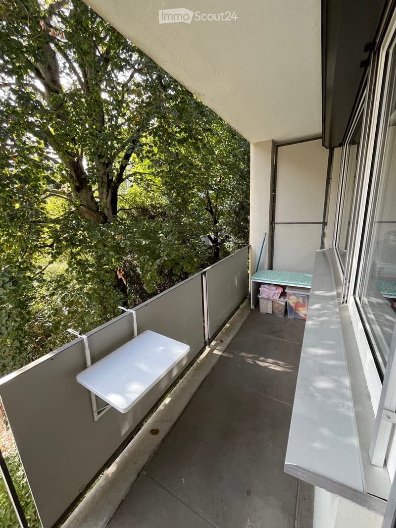 Balcony with a small white table, storage bins, and a view of greenery outside.