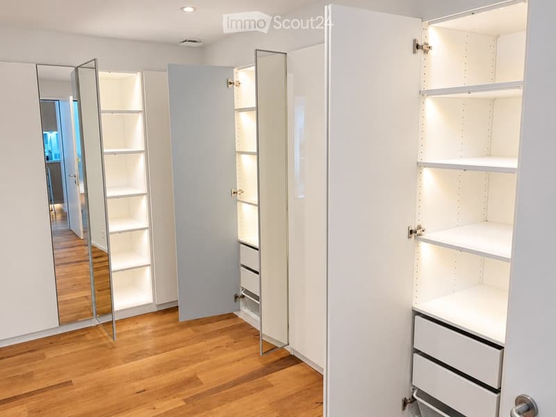 Empty room with white built-in wardrobes and mirrored doors, wooden flooring, and recessed lighting.