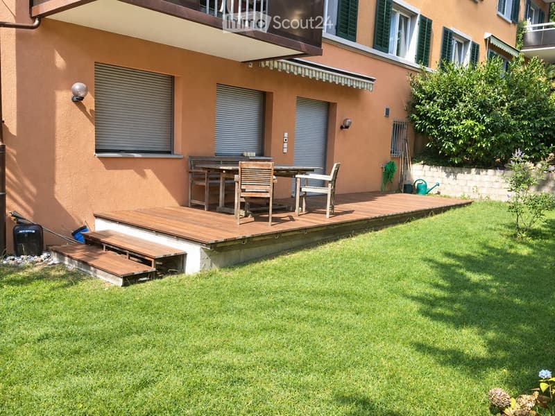 Wooden patio with a table and chairs, surrounded by a well-maintained lawn and garden area.