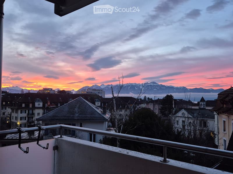 Balcony overlooking a cityscape with rooftops and distant mountains during sunset.