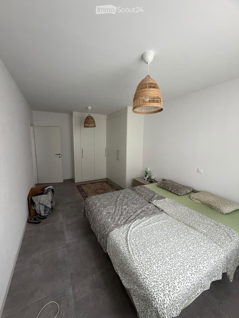 Modern bedroom with a double bed, nightstand, wardrobe, and pendant lamps.