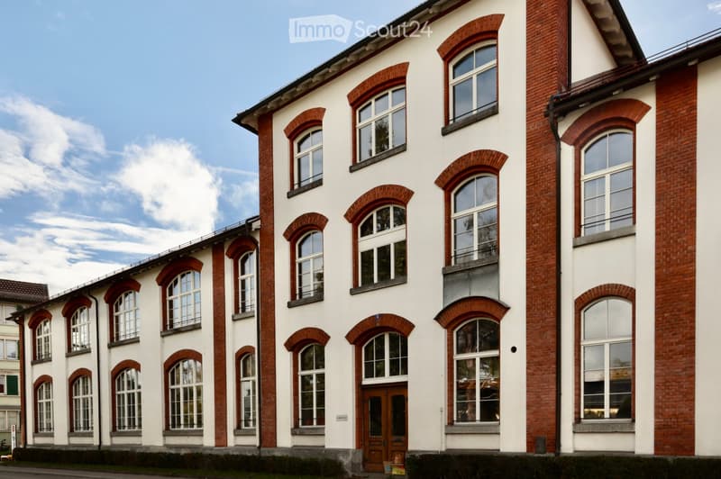 A multi-story building with white walls and red brick accents, featuring arched windows and a central wooden door.