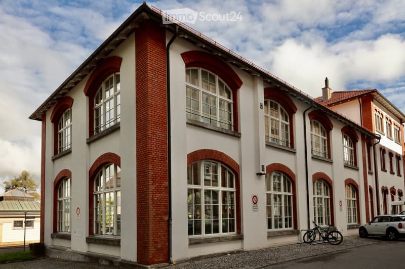 A multi-story building with red brick accents and large arched windows, featuring a flat roof and a modern design.