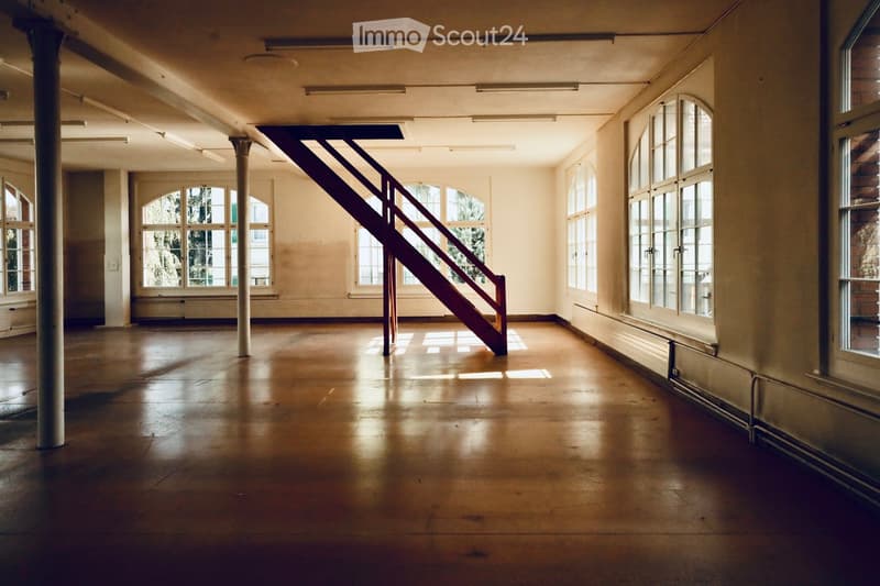 Empty room with wooden floor, large windows, and a staircase leading upwards. No furniture or equipment present.