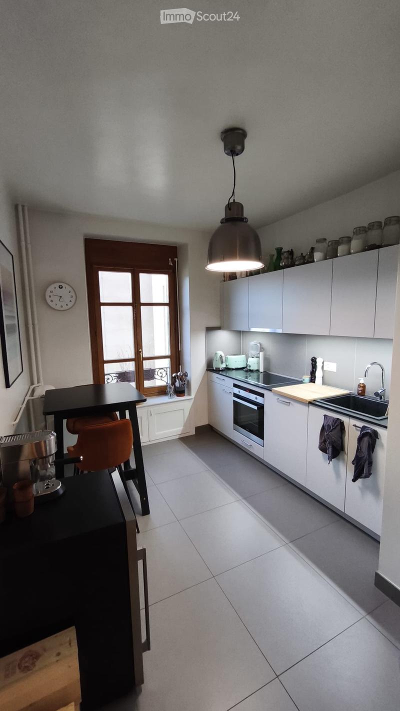Modern kitchen with white cabinets, stainless steel appliances, a black dining table with orange chairs, and a large window with wooden frame.