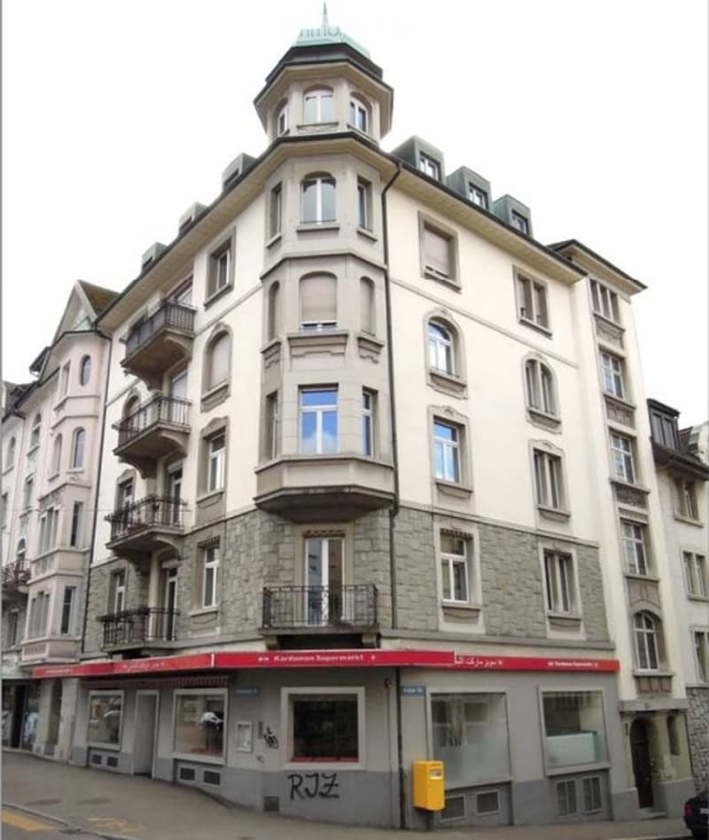 Multi-story building with balconies, large windows, and a red awning at the ground level.