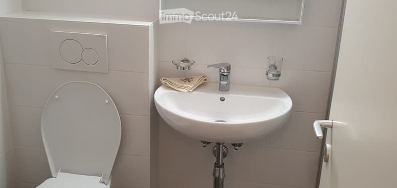 Modern bathroom with a white toilet, a sink with a chrome faucet, a folded towel, and a glass cup on the sink counter.