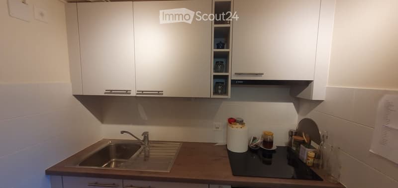 Modern kitchen with white cabinets, wooden countertop, stainless steel sink, and various kitchen items on the counter.