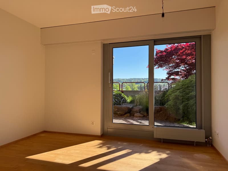 Unfurnished Room. Empty room with wooden flooring, large sliding glass doors leading to a garden area, and natural light streaming in.