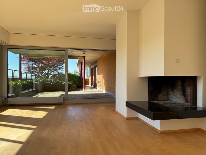 Living Room. Modern living room with light wooden flooring, large glass doors leading to a patio, and a built-in fireplace.