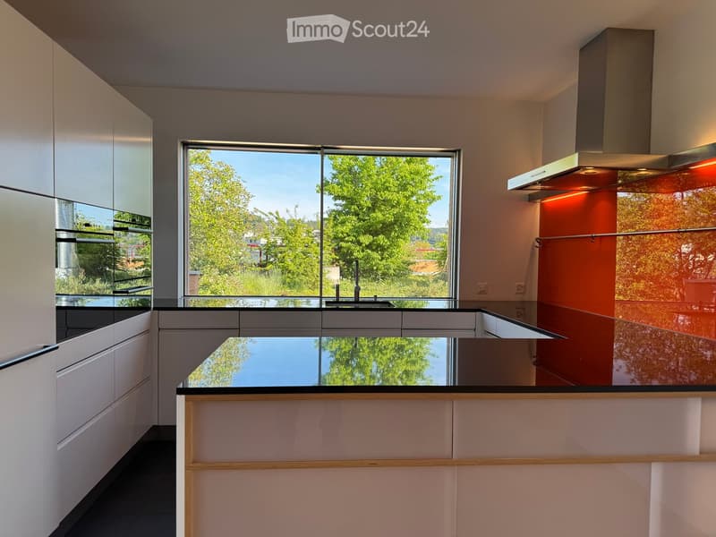 Kitchen. Modern kitchen with white cabinets, black countertops, a large window overlooking greenery, and a stainless steel range hood.