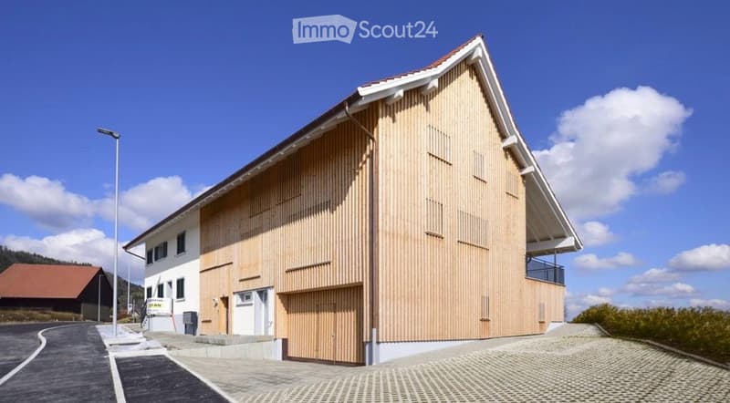 Modern two-story building with a wooden facade and white trim, featuring a garage and a balcony on the upper level.