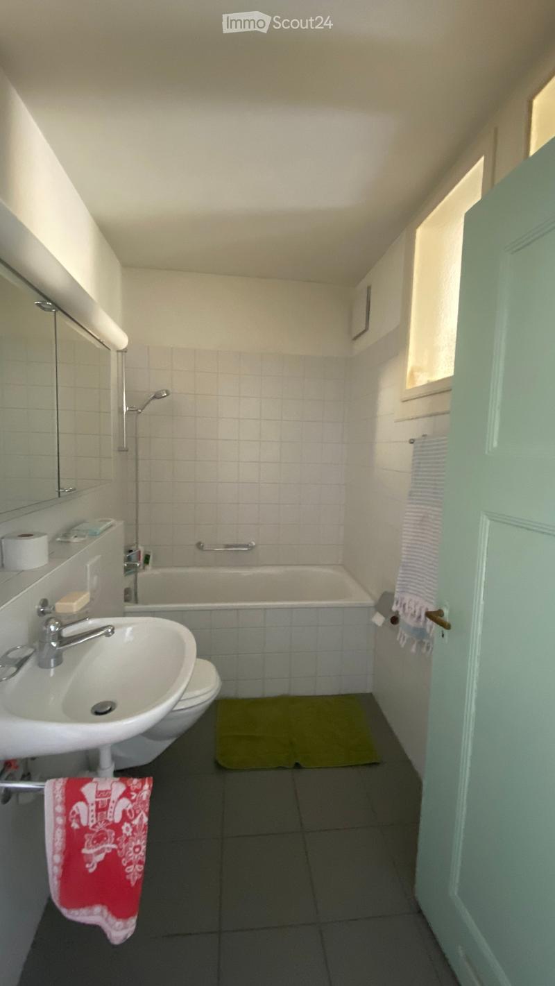 Bathroom with a sink, toilet, bathtub, and a small window. Includes a towel and a bathmat on the floor.