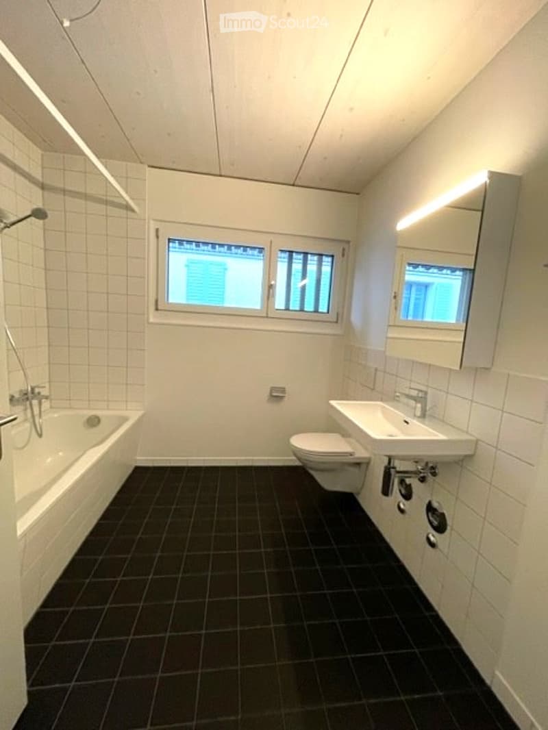 Modern bathroom with white tiled walls, black tiled floor, bathtub, toilet, sink, and mirror.