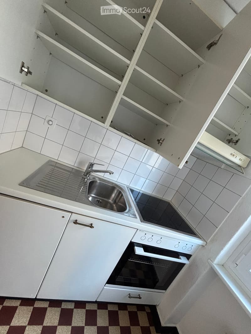 Empty kitchen with white cabinets, a stainless steel sink, and an oven. The cabinets are open, revealing empty shelves.