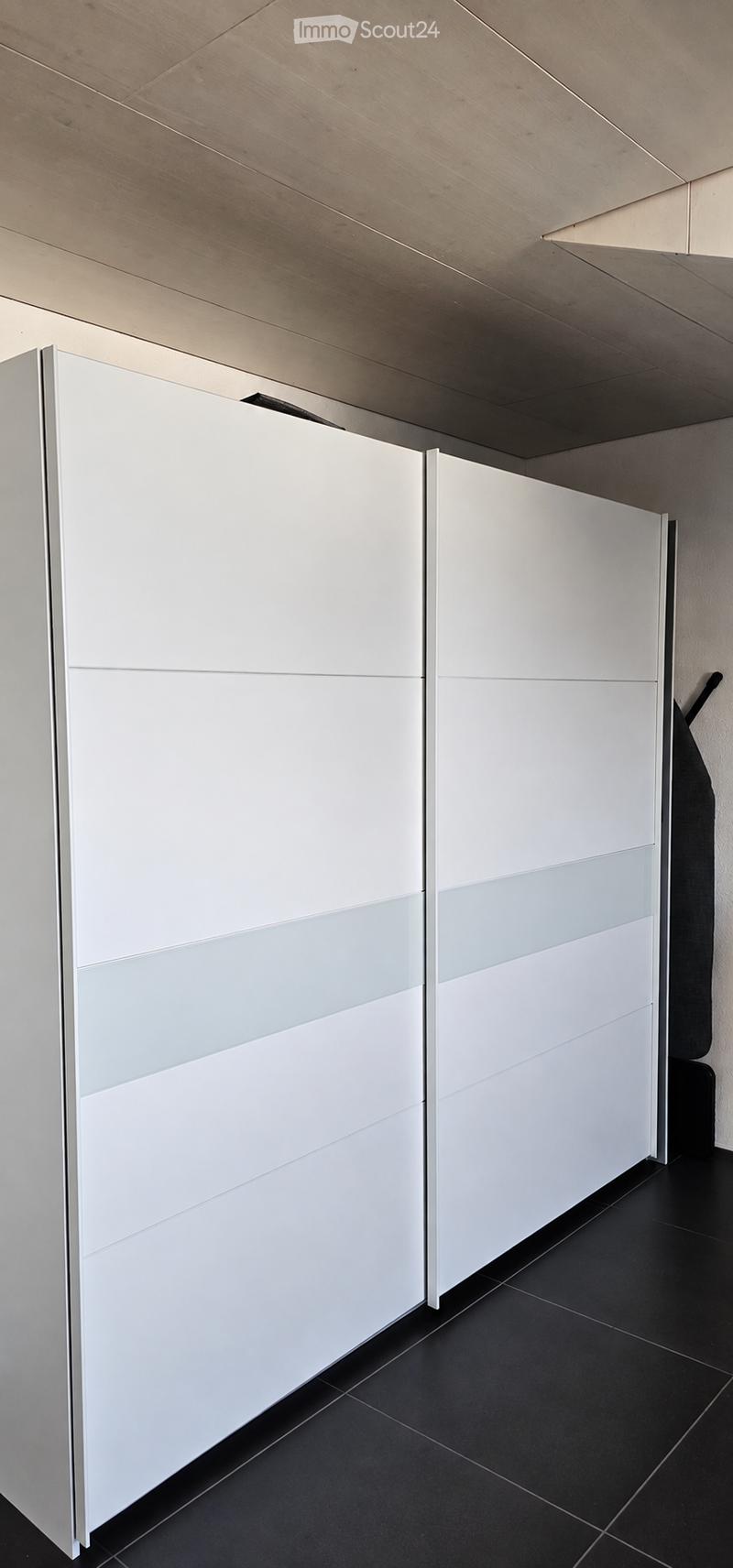 Modern, minimalist room with white sliding closet doors and black tiled flooring. The space is completely empty, with no furniture or personal items visible.