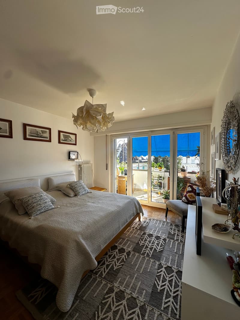 Bright bedroom with a large bed, patterned rug, modern lamp, and a view of the sea through large sliding glass doors.
