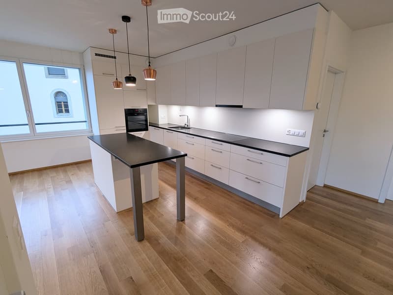 Modern kitchen with white cabinets, black island, wooden flooring, and pendant lights.