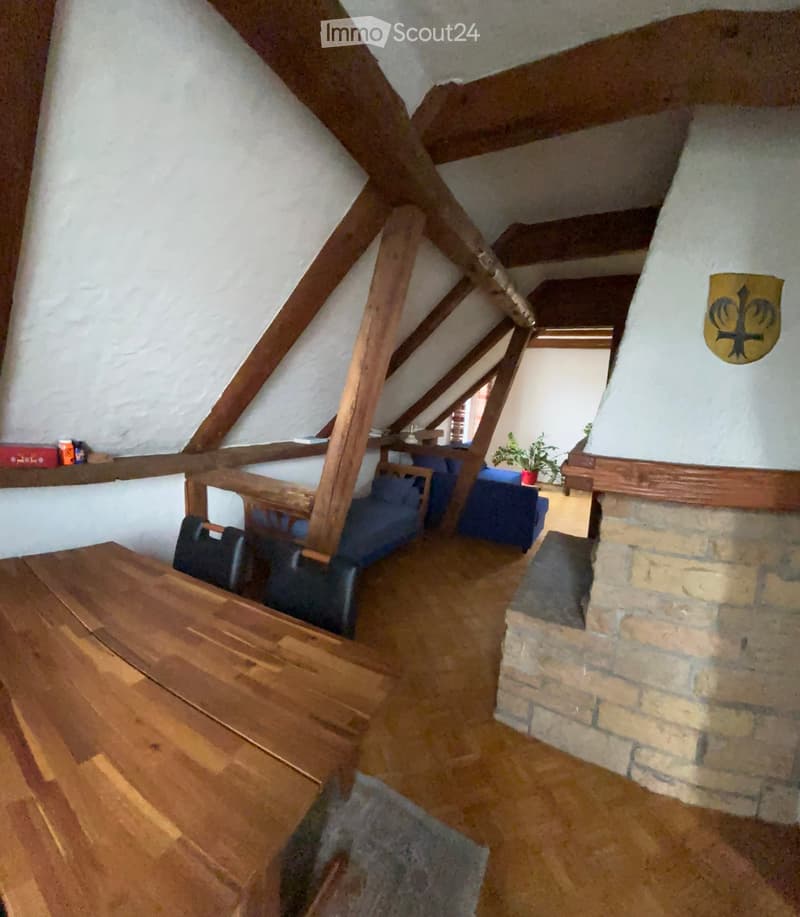 Attic room with wooden beams, exposed wooden ceiling, fireplace, wooden table, chairs, and a sofa.